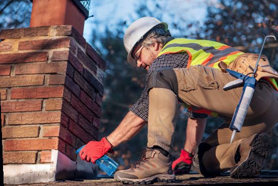 Roofer sealing chimney flashing at the shingle line on a Lakewood home