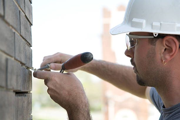 Close-up of a mason repointing mortar joints on dark brick in Lakewood