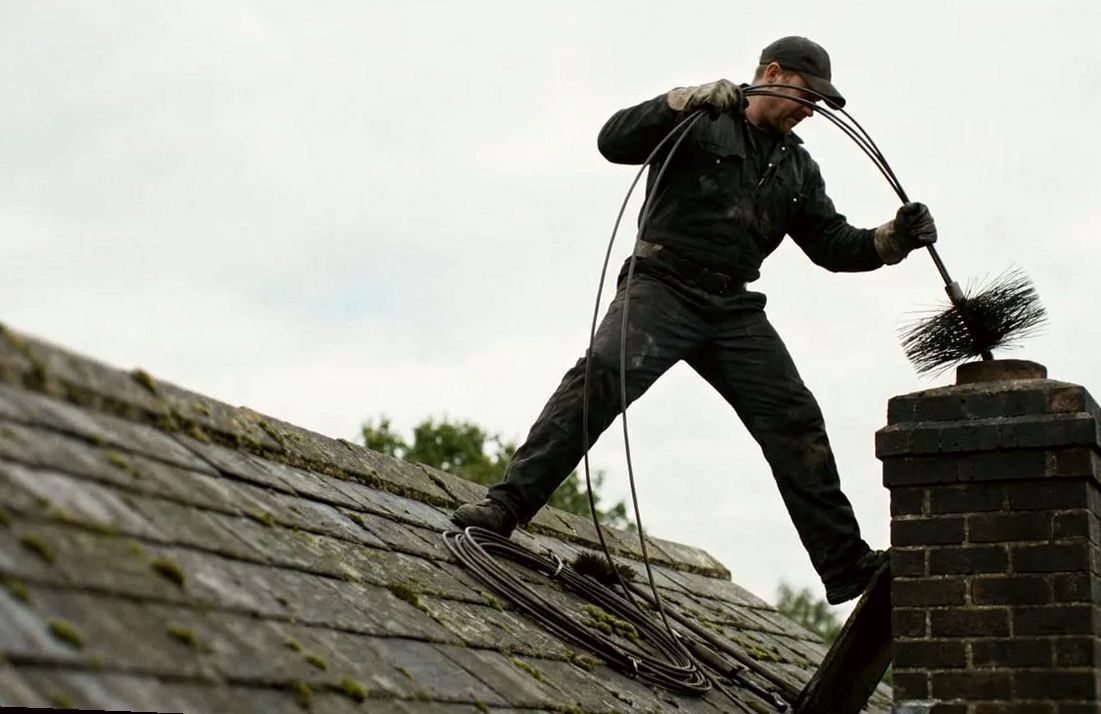 Chimney sweep driving a brush into a brick stack on a slate roof in Lakewood NJ